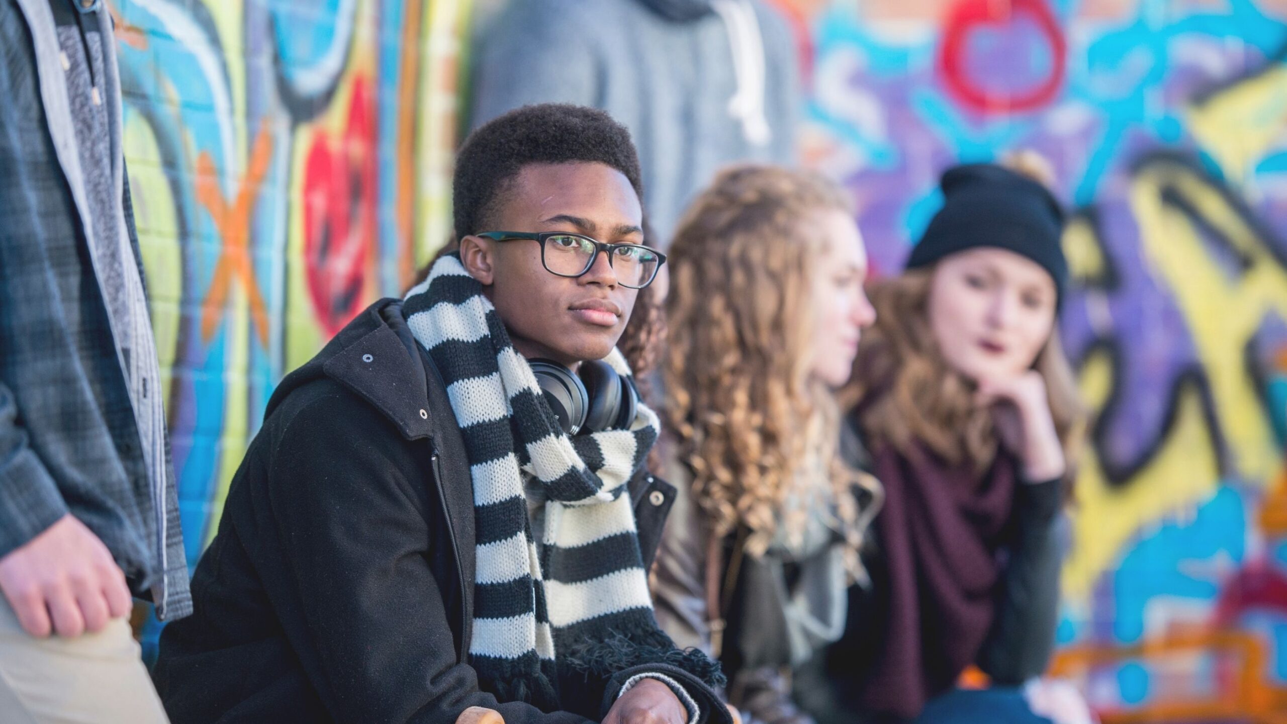 Young people are sitting in front of a graffiti wall.