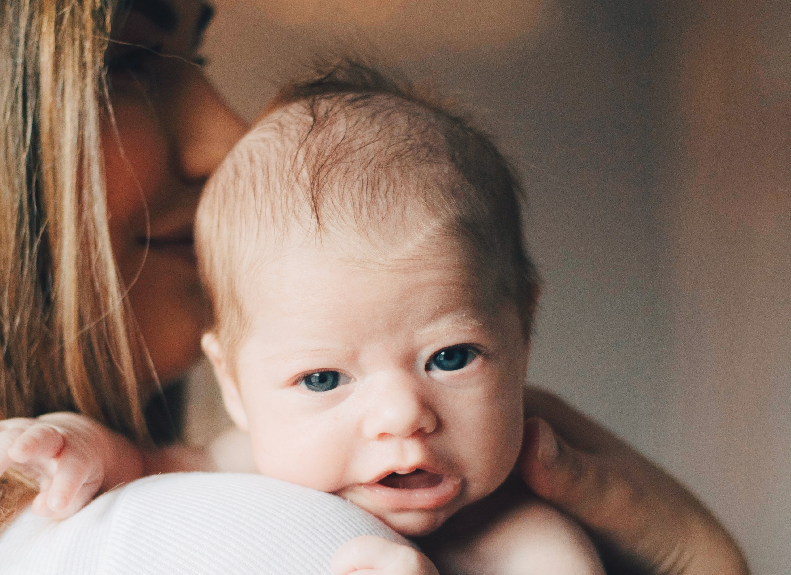 En liten baby är på en kvinnas axel och tittar rakt in i kameran.