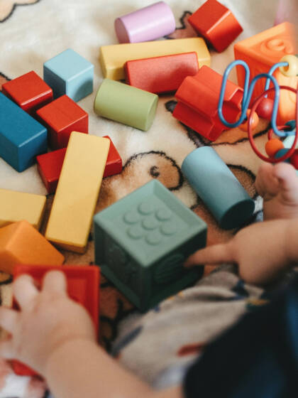 Taapero leikkii puupalikoilla ja muilla leluilla nallekuvioisen viltin päällä.