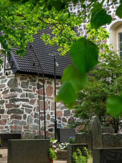Vanha kivikirkko vehreän puutarhan keskellä, hautakiviä etualalla.
