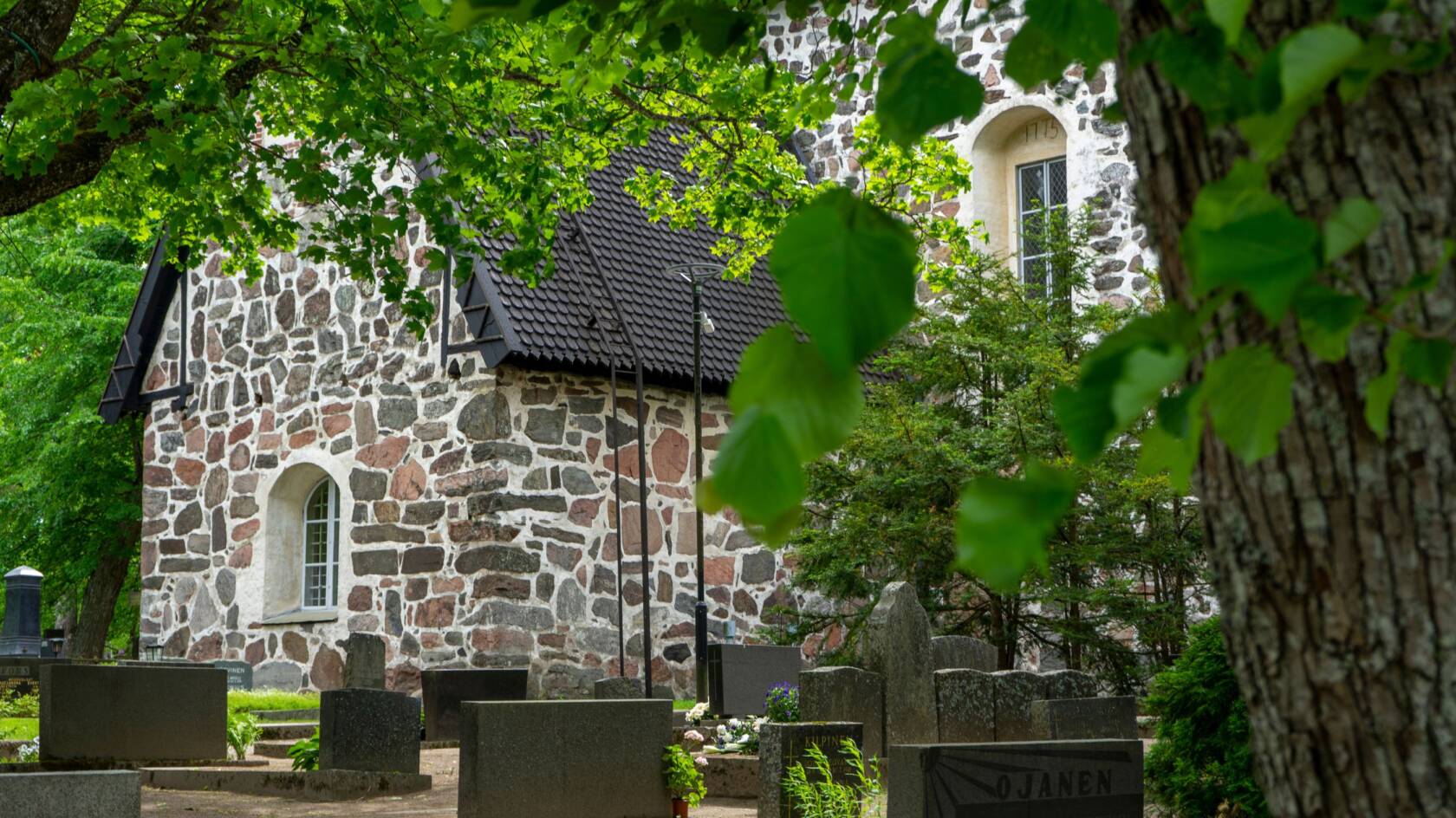 En medeltida stenkyrka på sommaren. Kyrkogården i förgrunden.