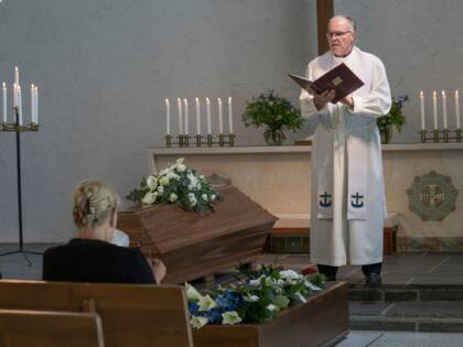 Pappi seisoo arkun takana siunaustilaisuudessa raamattu kädessä.