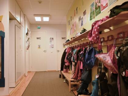En korridor i daghemslokalerna där barns färgglada kläder hänger på krokarna.