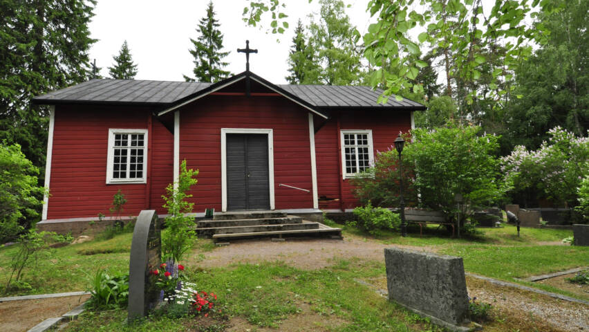 En liten röd träkyrka. Några gravstenar syns i förgrunden.