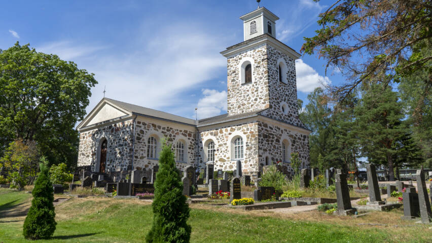 En ljus stenkyrka på sommaren med gravstenar i förgrunden.