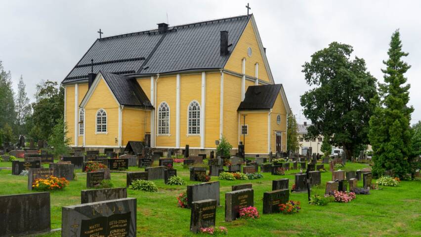 Keltainen puukirkko pilvisellä säällä.