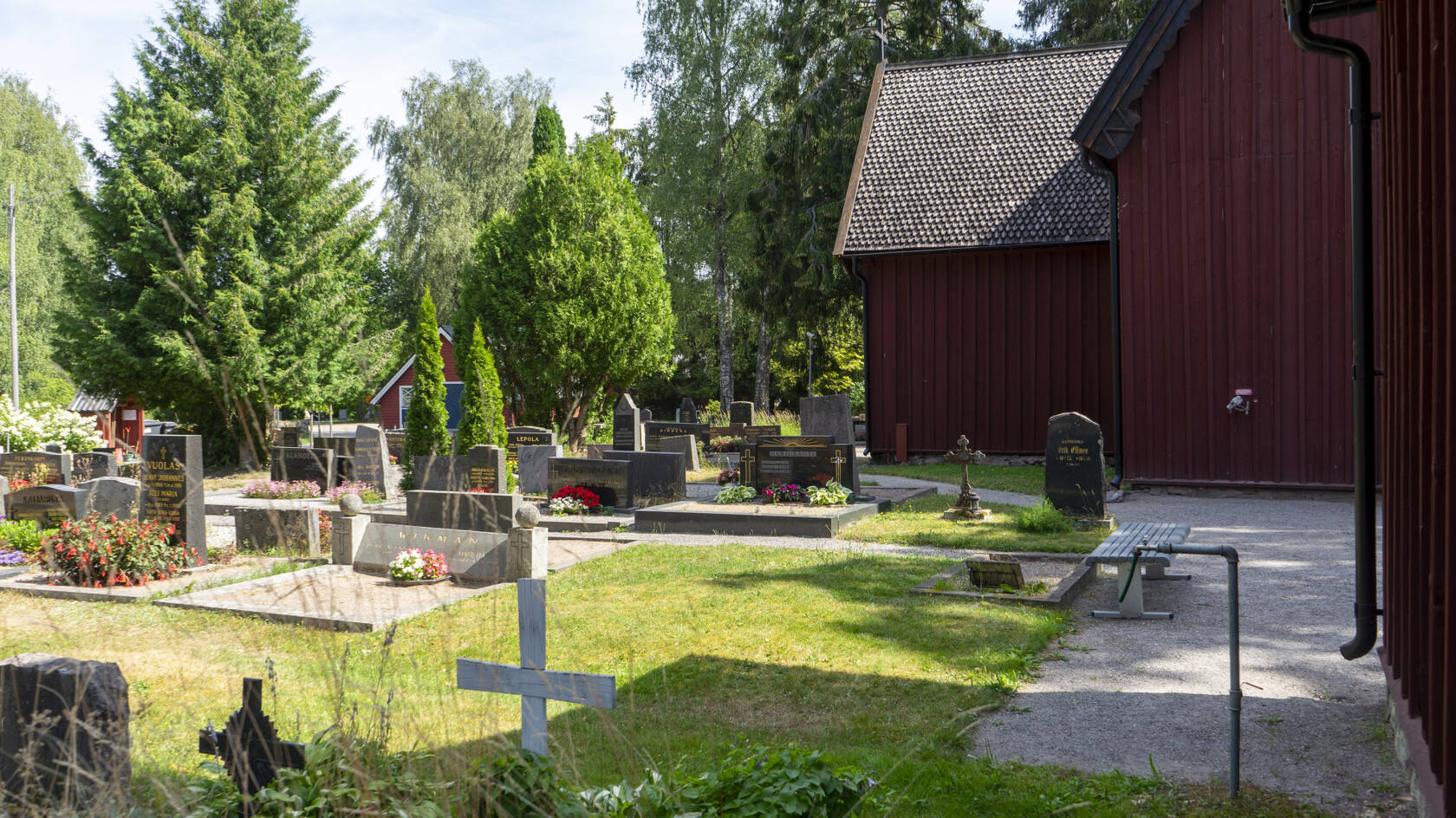 En kyrkogård. Till höger syns väggen av en röd träkyrka.
