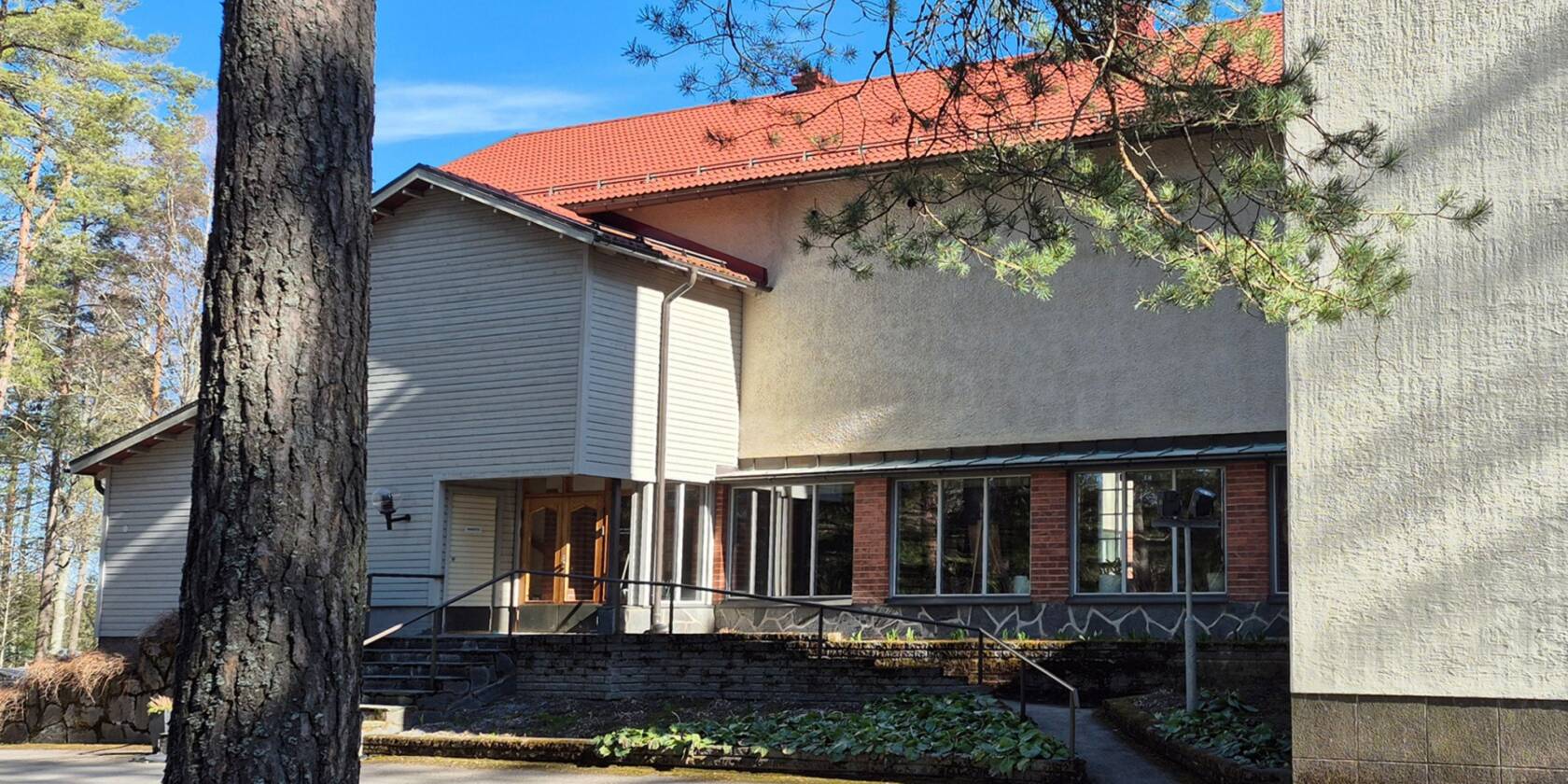 En ljus kyrka med rött tak fotograferad från sidan,. I vänstra kanten en trädstam.