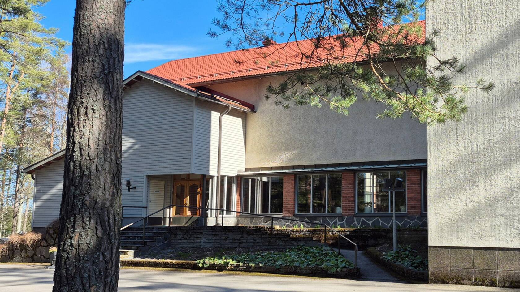 En ljus kyrka med rött tak fotograferad från sidan,. I vänstra kanten en trädstam.