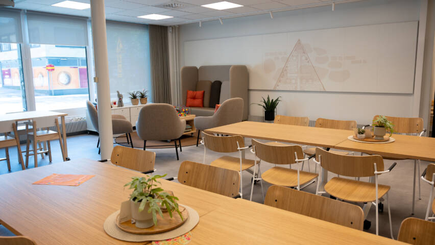 Sisäkuva, etualalla kaksi vaaleapintaista pöytää tuoleineen.