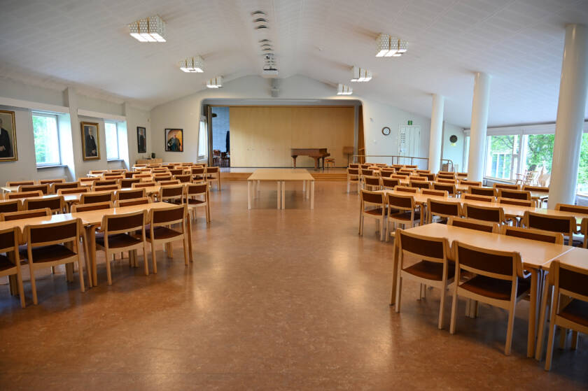 Seurakuntasalin sivuilla pöytäryhmiä tuolien kanssa. Edessä esiintymislava. Lavalla flyygeli.