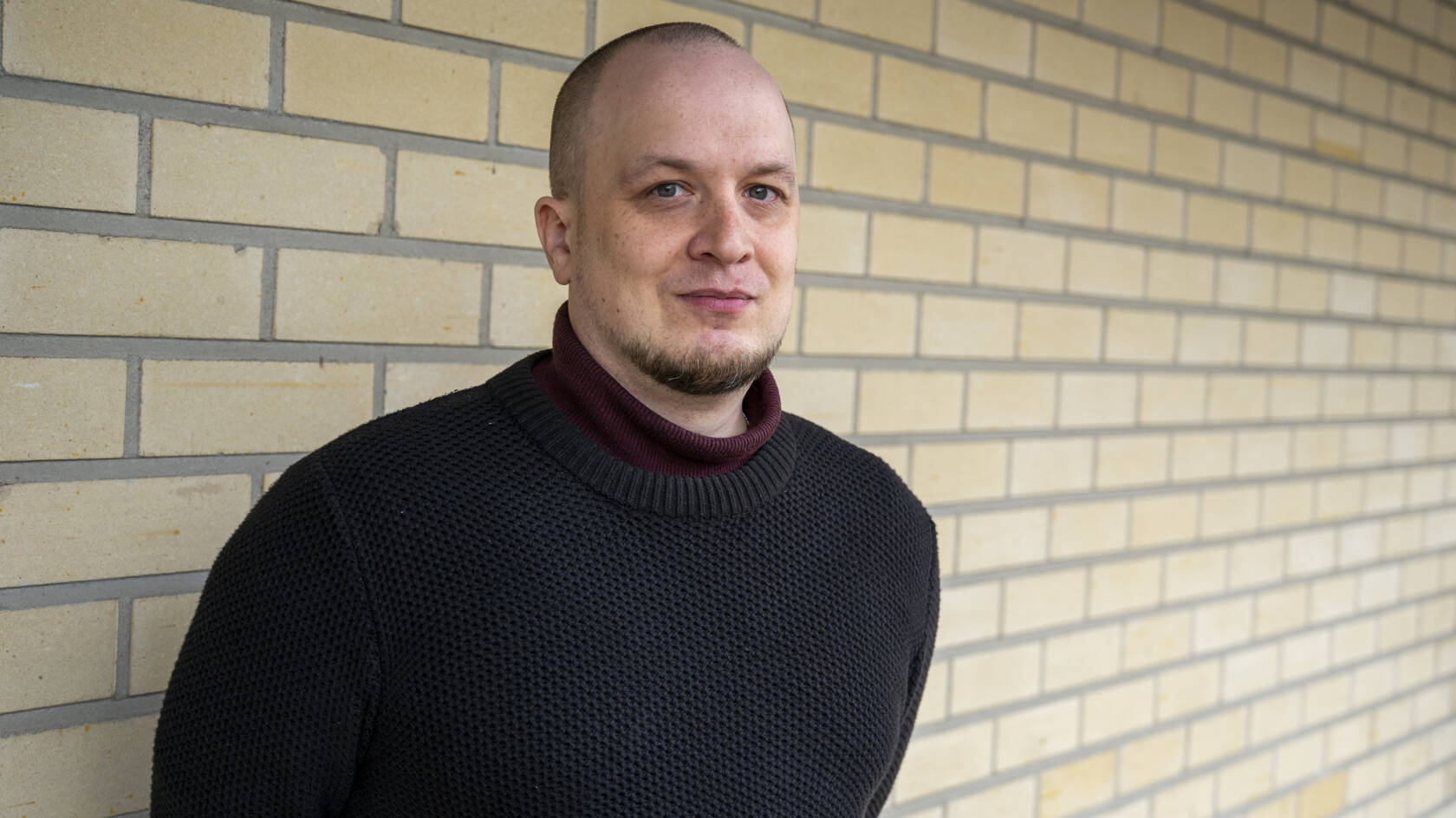 Mies seisomassa vaaleaa tiiliseinää vasten.