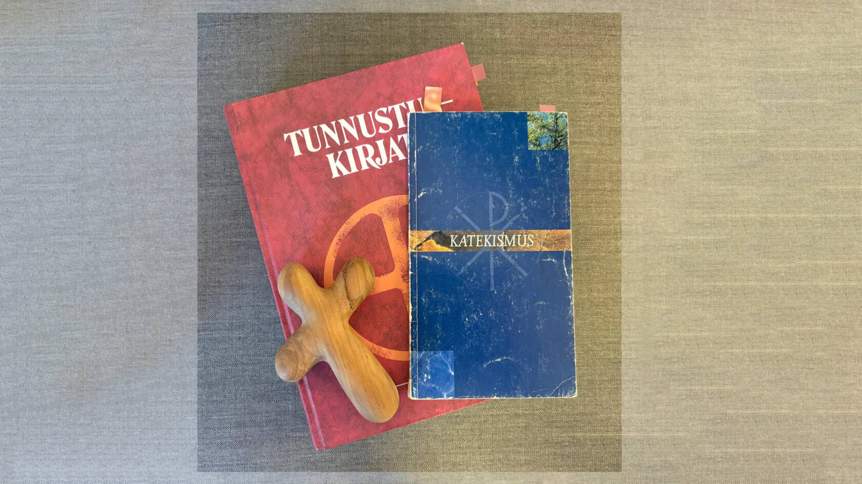 Kuvan keskellä punainen Tunnustuskirjat jonka päällä Katekismus ja puinen risti.