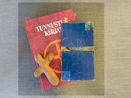 Kuvan keskellä punainen Tunnustuskirjat jonka päällä Katekismus ja puinen risti.