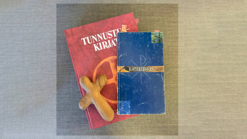 Kuvan keskellä punainen Tunnustuskirjat jonka päällä Katekismus ja puinen risti.